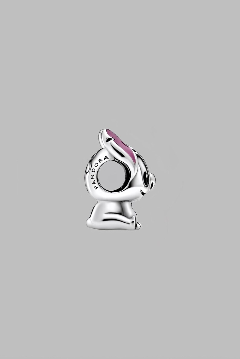 May include: A silver-colored charm in the shape of a cartoon bunny with pink accents on the ears. The charm has the word "PANDORA" engraved on the side. The bunny is sitting down with its head tilted slightly.