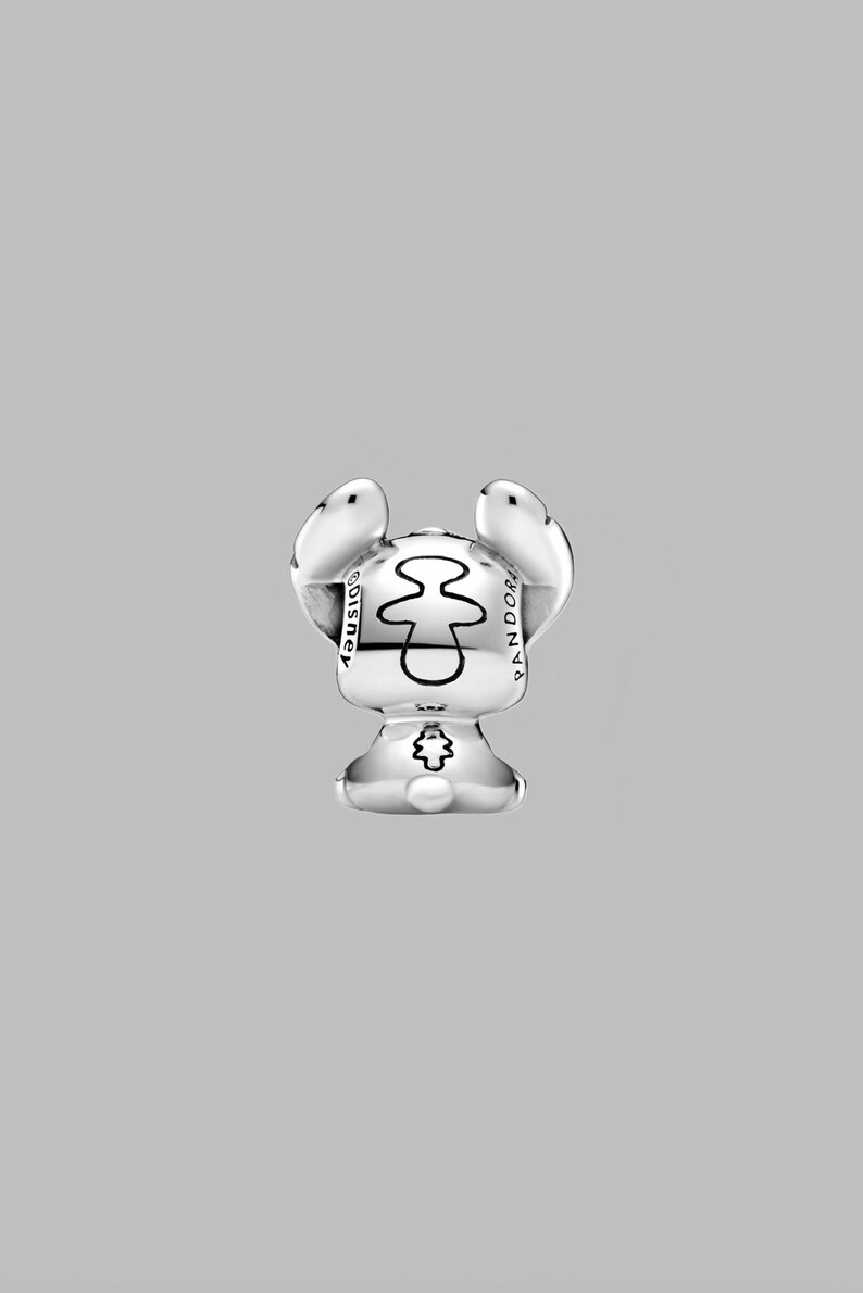 May include: A silver charm featuring a stylized character with large ears and a small body. The charm has the word "Disney" on one side and "Pandora" on the other. The character's design includes a central shape and a small emblem on the bottom.