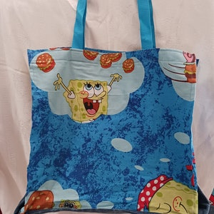 May include: A blue tote bag with a cartoon character of Spongebob Squarepants on it. The bag has blue handles and a denim trim.