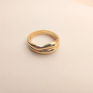May include: A gold-toned ring with a smooth, undulating wave-like design. The band features a polished, reflective surface and the word PANDORA is clearly engraved on the inner side of the metal band, visible from the top-down perspective.