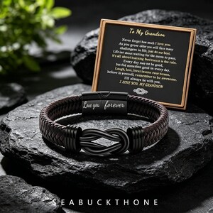 May include: A dark brown braided leather bracelet with a black metal infinity knot centerpiece and a magnetic clasp engraved with the words Love you forever. It is accompanied by a black card with gold text reading To My Grandson.