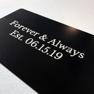 May include: A black rectangular card with rounded corners. The card features the words "Forever & Always" above "Est. 06.15.19" in a white, elegant font. The card is set against a white background.