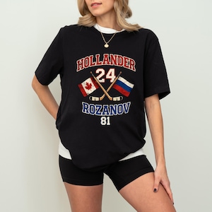 Könnte beinhalten: Schwarzes T-Shirt mit einem Hockey-Motiv. Das Design umfasst den Namen "HOLLANDER" über der Nummer "24", gekreuzte Hockeyschläger und den Namen "ROZANOV" unter der Nummer "81". Flaggen von Kanada und Russland sind ebenfalls abgebildet.