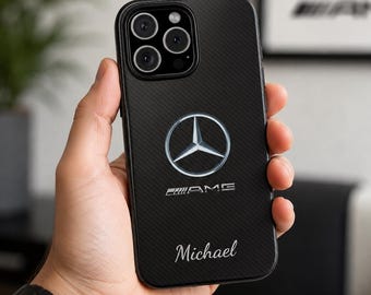 Puede incluir: Una funda de smartphone negra con textura de fibra de carbono diagonal, que presenta el logotipo plateado de Mercedes-Benz, el emblema AMG y el nombre Michael impreso en una fuente cursiva blanca. La funda tiene un recorte para la triple cámara.
