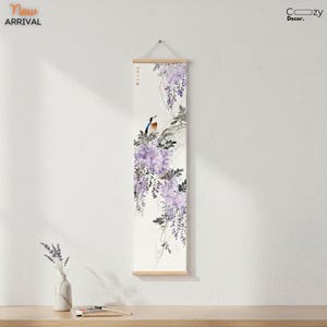 Puede incluir: Un colgante de pared vertical con una pintura de acuarela de un pájaro posado en una rama con flores de glicinas moradas. La obra de arte está montada sobre varillas de madera y se suspende con una cuerda. Las palabras "New Arrival" están en la esquina superior izquierda.