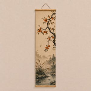 May include: A vertical wall hanging scroll featuring a painting of a tree branch with orange fruit extending over a landscape. The scene depicts a stream flowing through a misty forest with tall grasses in the foreground, all on a textured beige fabric.