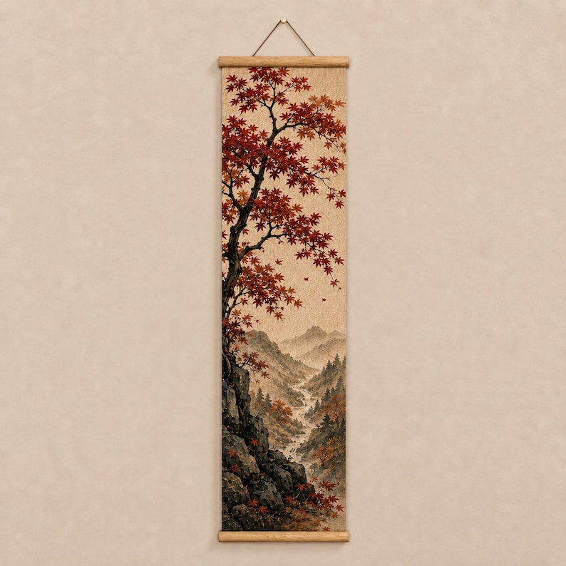 May include: A vertical wall hanging scroll featuring a detailed landscape painting. The artwork depicts a rocky cliffside with a large tree displaying vibrant red autumn leaves, overlooking a misty valley with distant mountains and a winding stream.