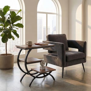 May include: A three-tiered side table with a dark brown tabletop and shelves, supported by black curved metal legs. A small sculpture sits on the bottom shelf. A mug and notebook rest on the top shelf. The table is next to a gray armchair.