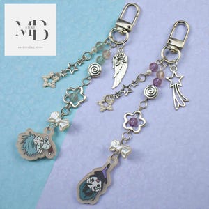 May include: Two keychains with silver-tone hardware, each featuring charms like stars, flowers, and angel wings. One keychain has a cartoon character charm. The other keychain has a cartoon character charm. The keychains have a variety of beads and a bow.