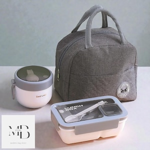 May include: A grey lunch bag, a white and grey food container, and a white and grey food container with a clear lid. The lunch bag has a handle and a panda logo. The food container has a clear lid with a spoon and the words "LUNCH BOX".