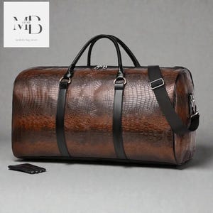 May include: A brown leather duffel bag with a crocodile skin texture. The bag has black handles, straps, and accents. A small black leather wallet is in front of the bag. The bag has the text "MD STORE modern bag store" in the upper left corner.