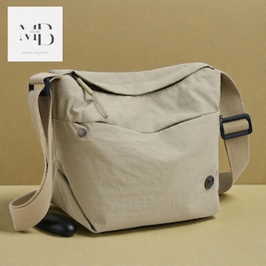 Puede incluir: Bolso mensajero beige con una correa larga y ajustable. El bolso tiene un cierre de solapa y un pequeño bolsillo en la parte delantera. El texto "MD STORE" y "modern bag store" está en la esquina superior izquierda.