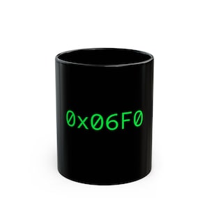 May include: A black ceramic mug with the text "0x06F0" in bright green. The mug is cylindrical and has a glossy finish. The text is centered on the front of the mug.