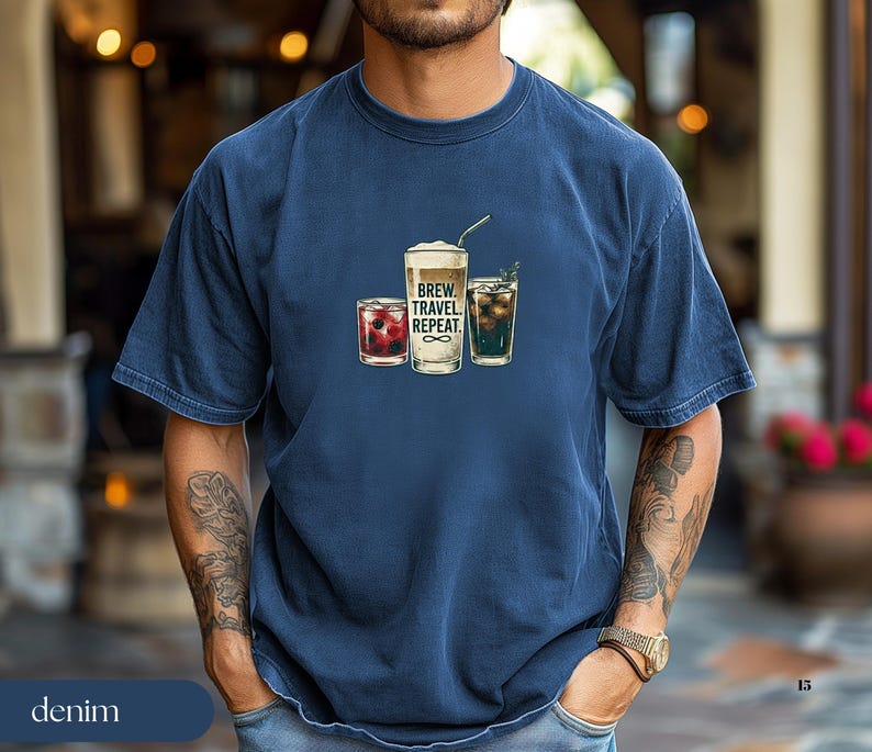 Puede incluir: Camiseta azul marino con un gr&aacute;fico de tres bebidas: una bebida de bayas, una bebida de caf&eacute; con pajita y una bebida verde. El texto "BREW. TRAVEL. REPEAT." est&aacute; impreso.