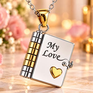 Puede incluir: Un colgante plateado con forma de pequeño libro que cuelga de una cadena. La cubierta presenta el texto grabado My Love y un pequeño emblema de corazón dorado. El lomo del colgante tiene anillos cilíndricos alternos en plata y oro.