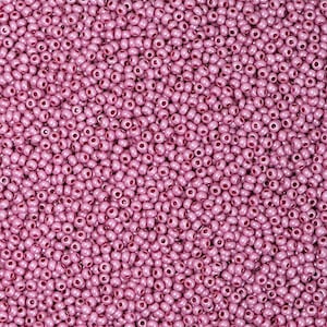 May include: A close-up shot of a mass of small, round, pink seed beads. The beads are consistent in size and shape, with a subtle sheen. They are tightly packed, forming a textured surface. Suitable for jewellery making and crafts.