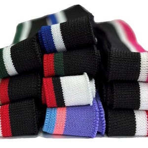 May include: A pile of black knitted wristbands with different coloured stripes. The bands have stripes in white, red, blue, green, pink, and tan. The wristbands are made of a textured knitted material.