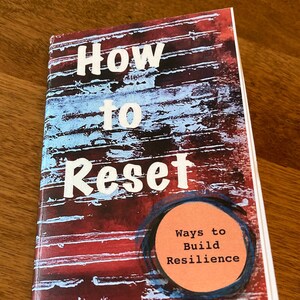 May include: A book titled "How to Reset" with a red, blue, and black abstract cover. The book's subtitle is "Ways to Build Resilience".