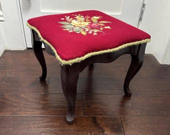Taburete de madera vintage con cojín tapizado con bordado floral y ribete trenzado.