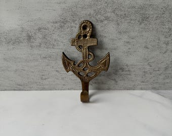 Op de afbeelding: Een bronzen anker-vormige wandhaak. De haak heeft een gedetailleerd ontwerp, inclusief de vloeien, de schacht en de ring van het anker. De haak is ontworpen om items op te hangen en is geschikt voor nautische thema-decoratie.