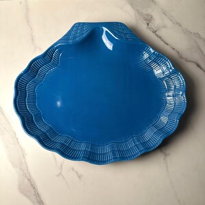 Może przedstawiać: Żywy, niebieski półmisek w kształcie muszli. Ceramiczne naczynie ma falisty brzeg i teksturowane detale. Półmisek ma jasnoniebieski kolor i idealnie nadaje się do serwowania przekąsek lub eksponowania elementów dekoracyjnych.