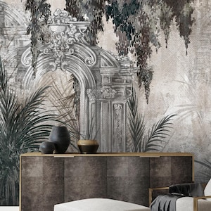 May include: A room interior featuring a mural with classical architectural elements and tropical foliage. A dark brown cabinet, a white armchair with a gold frame, and a matching ottoman are in front of the mural. Decorative vases are on the cabinet.