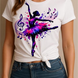 Op de afbeelding: Wit t-shirt met een ballerina-ontwerp, inclusief muzieknoten en een vioolsleutel. De tutu van de ballerina is een splash van paars, roze en blauw. Het t-shirt is in de taille geknoopt.