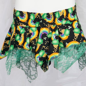 Pode incluir: Uma saia preta com estampa verde e dourada de arco-íris e potes de ouro. A saia tem uma bainha de renda verde.