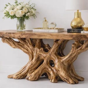 Puede incluir: Una consola de madera natural con una base única en forma de raíz. La mesa tiene un jarrón con flores blancas, una lámpara dorada y objetos decorativos. La mesa mide aproximadamente 152 cm de largo, 41 cm de ancho y 76 cm de alto.