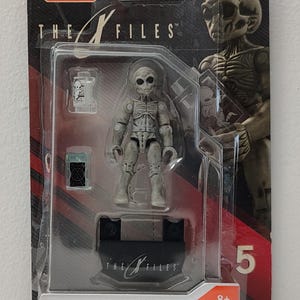May include: Mega Construx The X-Files action figure set featuring a gray alien figure and accessories. The packaging includes the text "The X-Files" and "Mega Construx". The set includes 17 pieces and is for ages 8 and up.