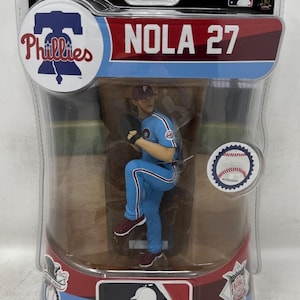 Puede incluir: Figura de béisbol del lanzador de los Phillies, Nola, con uniforme azul claro con el número 27. El embalaje incluye el logotipo de los Phillies y la marca MLB. La figura está en pose de lanzamiento.