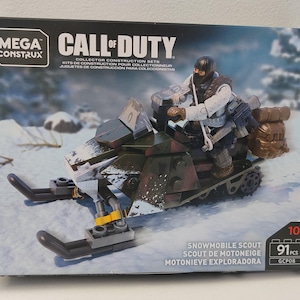 以下が含まれることがあります： メガコンストラックス コールオブデューティ スノーモービルスカウトのコレクター建設セット。箱には兵士のフィギュアが付いたスノーモービルが描かれています。スノーモービルは緑と茶色で、黒いスキーが付いています。セットには91個のパーツが含まれており、10歳以上向けです。