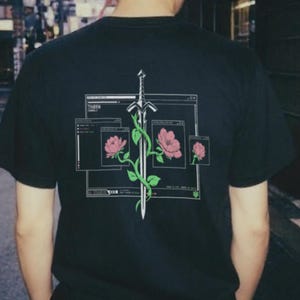 May include: A black short-sleeve t-shirt featuring a graphic on the back. The design displays a silver sword entwined with pink roses and green leaves, framed by white rectangular computer window outlines on a dark background.
