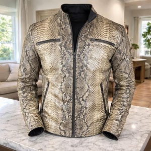 May include: A snakeskin-effect jacket with a black collar and zip. The jacket features two zipped chest pockets and two side pockets. The jacket is made of a reptile-like material with a beige and brown pattern.
