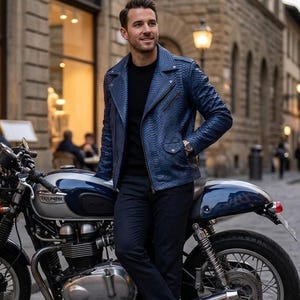 Peut inclure: Veste de moto en cuir bleu avec un motif texturé. La veste a une fermeture éclair et est portée sur un t-shirt noir. La personne est appuyée contre une moto Triumph bleue et argentée.