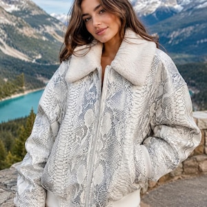 May include: A zip-up bomber jacket featuring a grey and white snakeskin pattern, a cream-colored faux fur collar, and ribbed cuffs at the sleeves and hem. The jacket has a central zipper closure and two side pockets, providing a structured fit.