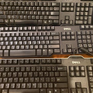 May include: Three black Dell computer keyboards arranged vertically. Each keyboard features a standard QWERTY layout, a numeric keypad on the right side, function keys along the top, and the Dell logo printed in white above the arrow keys.