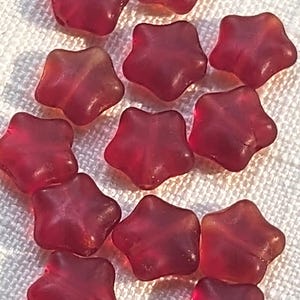 May include: A collection of translucent, star-shaped beads in a deep red hue. The beads have a slightly irregular shape, with rounded edges and a glossy finish. These decorative beads are suitable for jewelry making and craft projects.