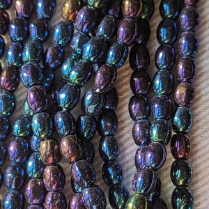 May include: A strand of iridescent oval-shaped beads in shades of blue, purple, and green. The beads have a metallic sheen and are strung on a clear thread.