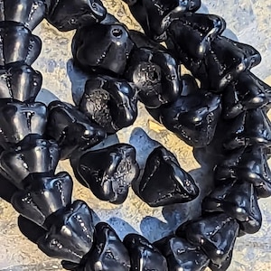 May include: Close-up of a necklace made of glossy, black, irregularly shaped beads. The beads are strung together, forming a circular pattern. The background is a light, textured surface, providing contrast to the dark beads.
