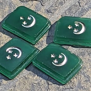 Pode incluir: Quatro azulejos quadrados verdes com um desenho de lua crescente prateada e três estrelas.