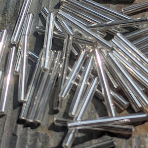 May include: A collection of clear, cylindrical glass tubes. The tubes are scattered across a textured, dark surface, with light reflecting off their smooth, transparent surfaces. The ends of the tubes appear to be sealed.