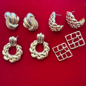 May include: A collection of gold-toned earrings in various styles, including knot, woven hoop, and square designs. The earrings are displayed on a vibrant red background, showcasing their metallic sheen and diverse textures. These earrings are perfect for adding a touch of vintage glamour.