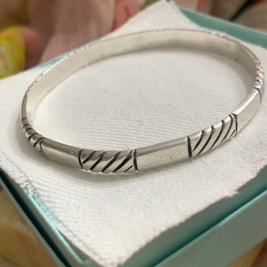 May include: A silver bangle bracelet with a braided design. The bracelet is simple and elegant.