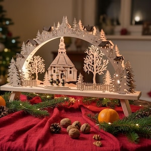 Könnte beinhalten: Ein hölzerner Weihnachtsbogen mit Kirche, Bäumen und Häusern. Der Bogen ist mit Lichtern beleuchtet und steht auf einem Tisch mit Orangen, Tannenzapfen und Walnüssen. Verschwommener Hintergrund mit Weihnachtsbaum.