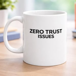 May include: White ceramic mug with the text "ZERO TRUST ISSUES" in black. The mug has a curved handle and is sitting on a wooden surface. The mug is a standard size for coffee or tea.