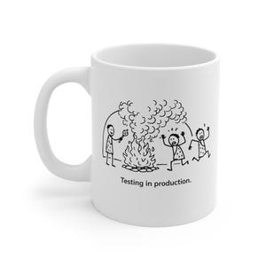 May include: White ceramic mug featuring a black and white cartoon depicting three stick figures near a fire. One figure holds a torch, while the others flee. The text "Testing in production" is printed below the illustration on the mug.