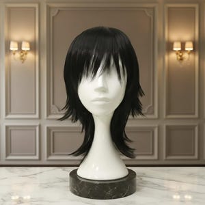 May include: A black wig with layered, shaggy bangs and side pieces is displayed on a white mannequin head. The mannequin is mounted on a dark, circular base. The wig is styled to frame the face.