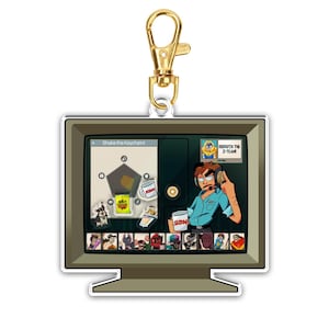 May include: A keychain featuring a cartoon design of a retro computer monitor with a gold-colored clasp. The monitor displays a cartoon character wearing a headset and the text "Dispatch the Z-Team". The keychain also has the text "Shake the Keychain!"