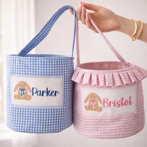 May include: Two Easter baskets, one blue and one pink, with gingham patterns. Each basket has a rectangular patch with a bunny and a name: "Parker" on the blue basket and "Bristol" on the pink one. Both have handles.